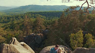 Good-looking young people in a casual wear. Adorable young lovers are lying on the mountain stone surrounded by forest