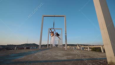 Air gymnastics woman hanging on aerial hoop on the roof with a nice view