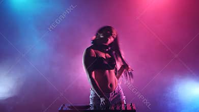 Girl dj hand spinning a dj stand, behind her pink blue lights in smoke