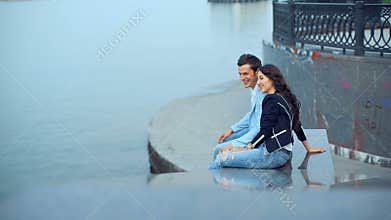 Young couple talking with smile while sitting near the river at the embankment