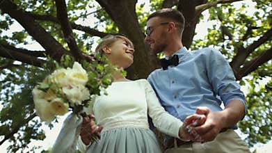 Bottom view. Young beautiful newlyweds kiss against a background of green tree in the park