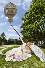 Woman in Venetian costume lying on the green park holding an old balloon