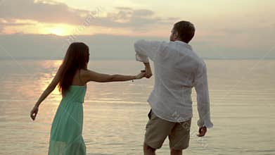 Young happy couple dancing on the beach on the sunset. Concept of love.