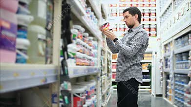 Man in dye shop. Rows of shelves with paint cans.