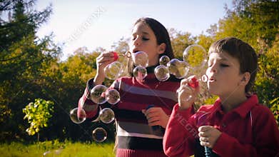Two kids blowing up the soap bubbles in autumn forest