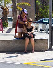 A young woman has her hair braided and plaited by a local street trader in Playa Las Americas in the Canary Island of Teneriffe