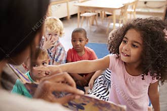 Pupils At Montessori School Looking At Book With Teacher
