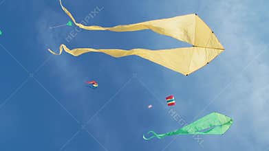 Yellow kite with two tails in flight against blue sky and sunny day