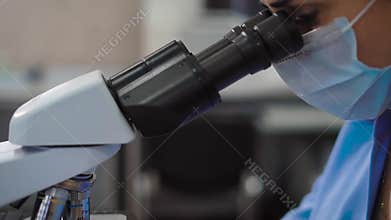 Crop shot of laboratory worker using microscope. Crop faceless shot of female specialist in uniform using microscope.
