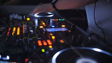 A DJ behind the console, on stage, mixing tracks in atmospheric dance party strobing and flashing lights.