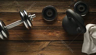 Top view of black iron kettlebell, dumbbell and white towel on w