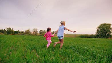 Two cheerful carefree kids hold hands. Together they run along the green meadow, having fun