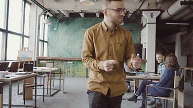Happy young man in cheerful mood walking through the office and dancing crazy. Businessman greets with colleagues.