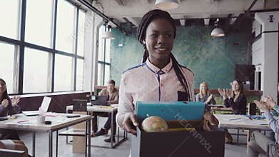 Young african woman recently hired for corporate job comes into new office. Female holds box with personal belongings.