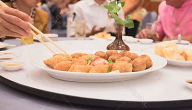 Fried food on dining table with hand holding chopsticks to pick up meatball inside restaurant background.