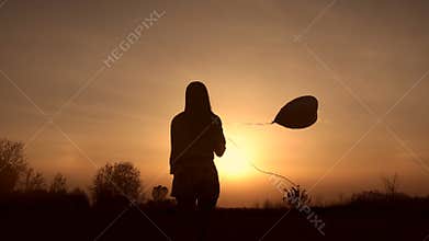 Silhouette of young woman with balloon at sunset