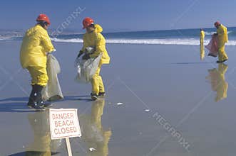 A sign warning, danger�beach closed with cleanup crews in the background