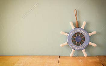 Old nautical wood wheel, anchor and shells on wooden table over wooden background. vintage filtered image