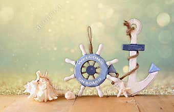Old nautical wood wheel, anchor and shells on wooden table over abstract glitter background
