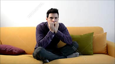 Young man watching TV, changing channels scared