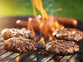 Hamburgers and hotdogs cooking on flaming grill
