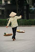 A woman is transporting goods in baskets in a street of Hanoi (Vietnam)