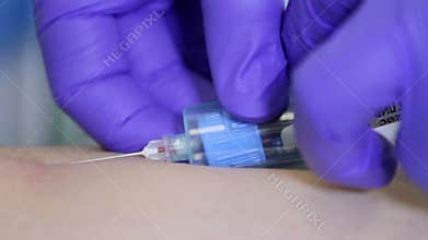 Doctor drawing blood sample from arm in blue tube
