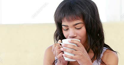 Smiling woman drinking hot beverage on bed