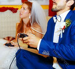 Bride and groom playing together videogames with joysticks - gaming and wedding concept.