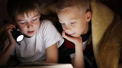 Two boys at night under a blanket reading a book