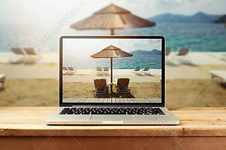 Laptop computer with sunny beach image on wooden table. Summer vacation photo