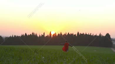 Boy with a superhero cape runs in a field during sunset