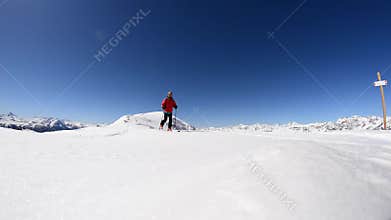 Alpinist ski touring on the ridge with expansive snowcapped mountain view in a bright sunny day.