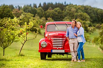 Senior couple hugging, vintage styled red car, sunny nature