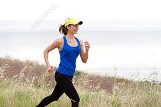 Athletic woman trail running by sea in baseball cap