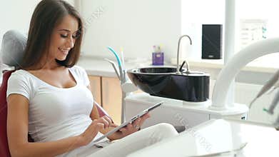 Woman in dentist chair taking tablet and smiling aside
