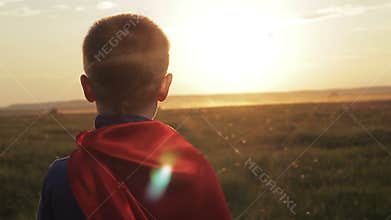Boy superhero in a field at sunset
