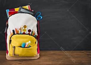Backpack full of school supplies over black school board background