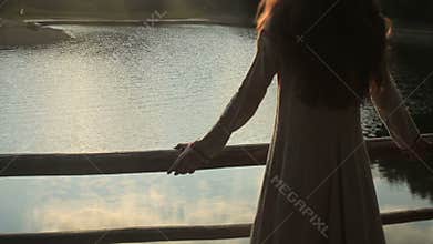 Close up of beautiful brunette young girl with sun in her hair. Young forest nymph standing on the pier and enjoy the