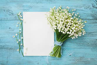 Bouquet of flowers lily of the valley and empty paper sheet on turquoise rustic table from above, beautiful vintage card, top view