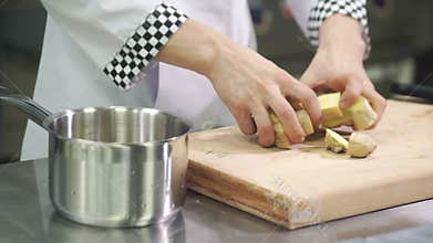 Cook adds coarsely chopped ginger root in pot in industrial kitchen