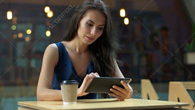Working at the cafe. Young beautiful long hair woman sitting at the table and using tablet computer in outdoor cafe