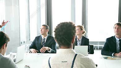 Business people sitting at table while female colleague giving presentation