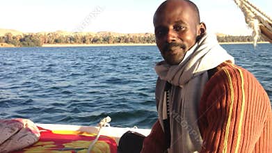 Nubian man looking a camera and talking while sailing felucca on the Nile