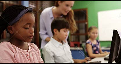 Teacher assisting school kids on personal computer in classroom