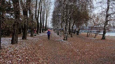 Girl running in autumn park during cold cloudy day. Woman exercising outdoors